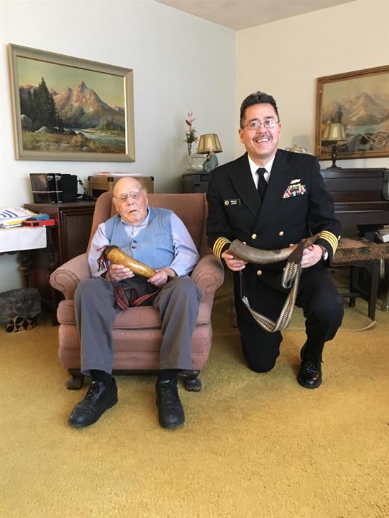 Two men, one elderly and one in military uniform, share a moment in a comfortable living room.