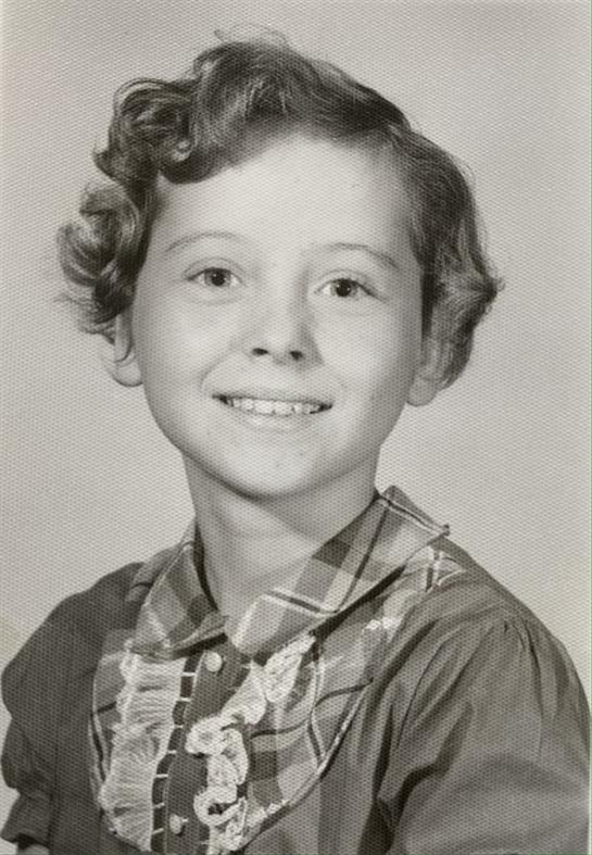 A cheerful girl smiles for a portrait, showing her curly hair and checked dress.