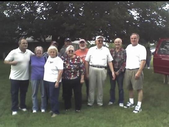 A group of adults stands together smiling in a park, enjoying a sunny day outdoors.