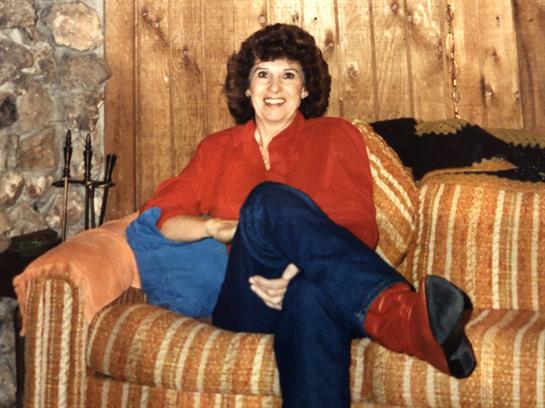A smiling woman enjoys her time seated on a striped couch with wooden walls around her.