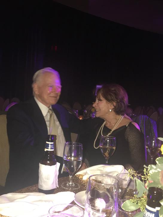A couple engages in a lively conversation while attending a formal gala dinner with beautiful decor.
