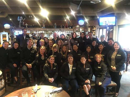 A group of smiling individuals in professional attire poses together at a restaurant.