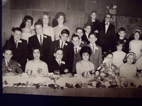 Children and teens dressed formally celebrate together with a decorated table in a banquet setting.