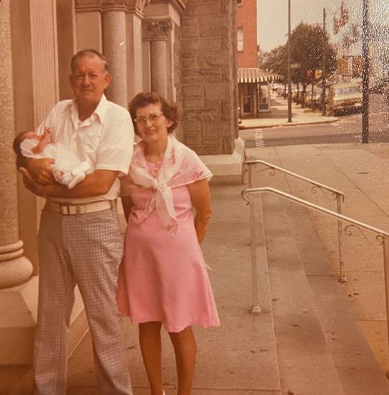 Family stands together outside a historic building, smiling and enjoying the sunny day.