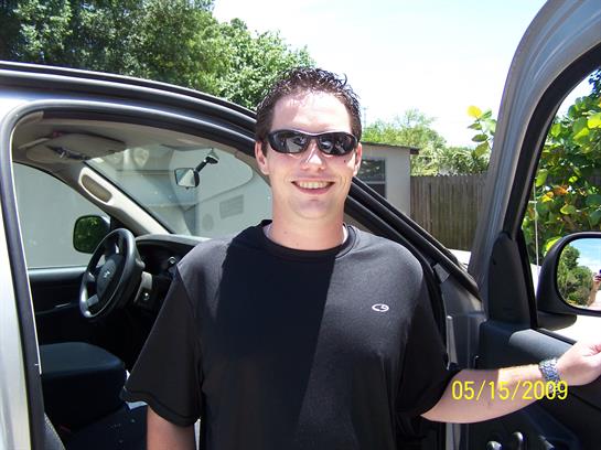 Bright sunny day with person enjoying time next to a black SUV, wearing sunglasses and smiling.
