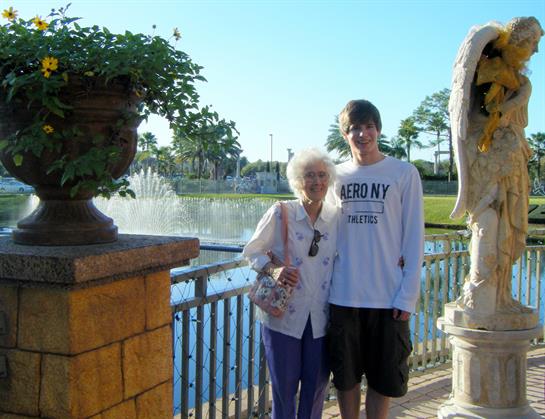 Elderly woman and young man smile by a stone, with a fountain in the background.
