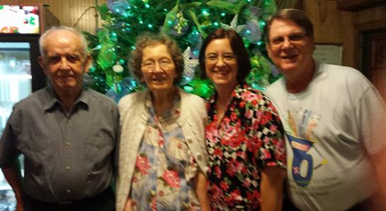 Family members stand smiling in front of a brightly lit Christmas tree, enjoying the holiday spirit.