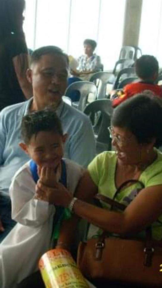 A grandmother playfully interacts with her grandson at a community event in a hall.