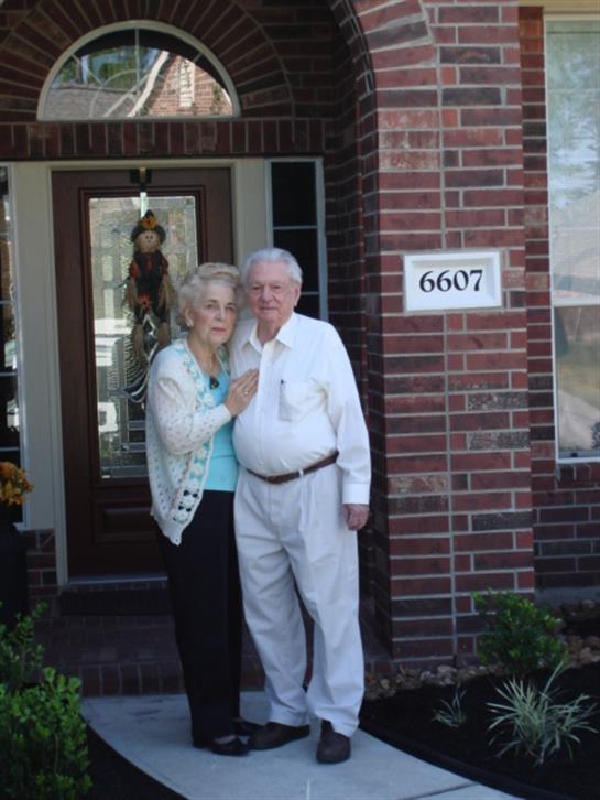 An elderly couple poses together at their residence, sharing a moment of joy and affection.