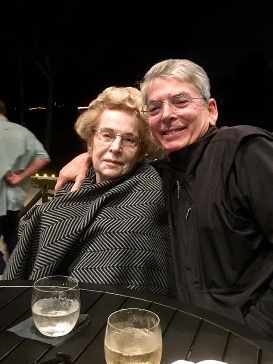 A couple sits closely together wrapped in a blanket, enjoying drinks at an outdoor event.