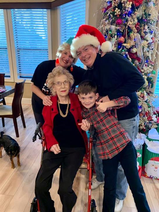 Family members gather around an elderly woman wearing festive attire in a cheerful holiday setting.