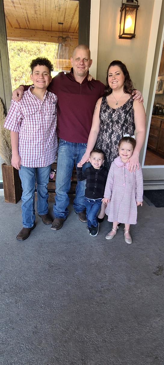 A family enjoys time together outside their home, smiling in the bright daylight.