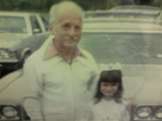 An elderly man and a young girl smile together outside on a sunny day.