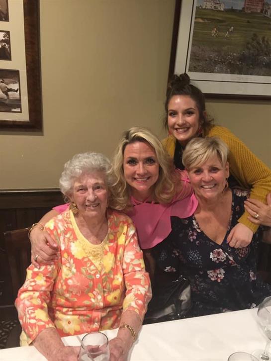 Four women share laughter and hugs while enjoying a meal together in a warm restaurant setting.