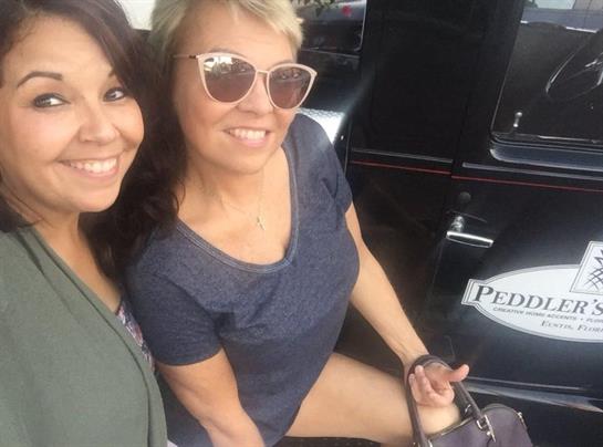 Two women smile brightly while seated in a rickshaw, enjoying a sunny day outdoors.