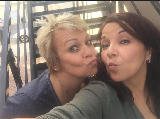 Two women pose happily, making funny faces while standing on a staircase outside.