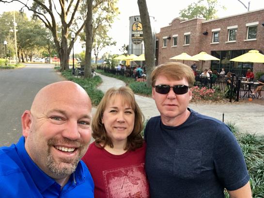 Friends enjoy a cheerful moment outdoors at a cafe, capturing smiles and camaraderie in the sun.