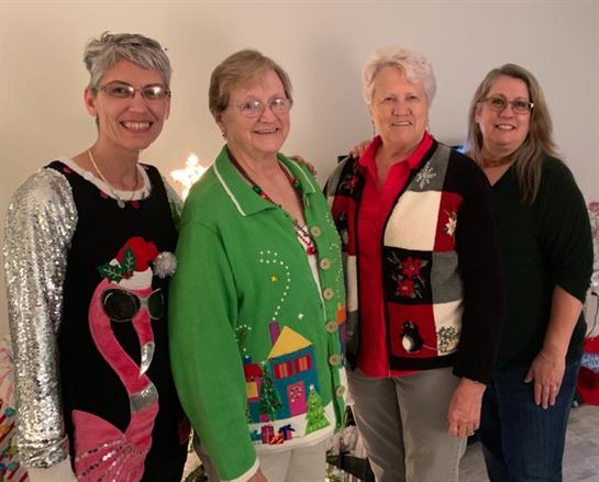 Four friends gather for a holiday celebration, showcasing their fun and festive sweaters together.