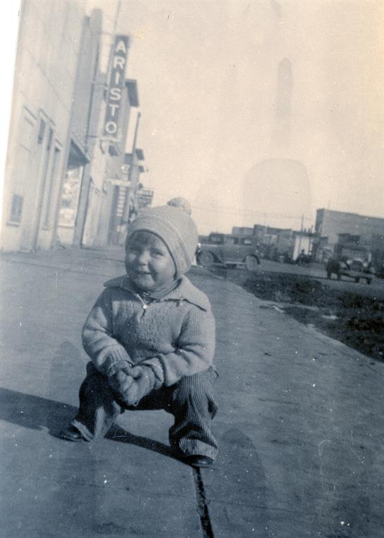 A joyful child is squatting on the sidewalk, wearing winter clothing in a city environment.
