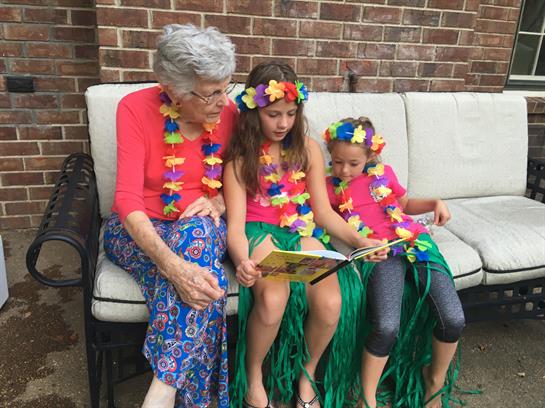 Three family members read joyfully in colorful festive outfits in a cozy outdoor space.