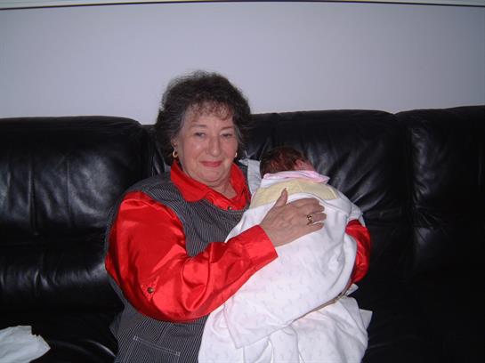 A grandmother gently holds her newborn grandchild on a cozy black leather couch.