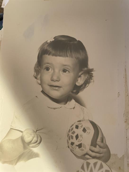 A young child smiles while holding a soccer ball in a nostalgic and warm black and white tone.