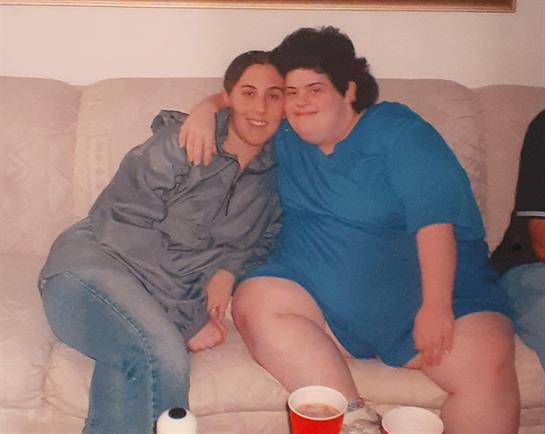 Two friends smile and enjoy their time together on a couch, surrounded by casual decor and drinks.