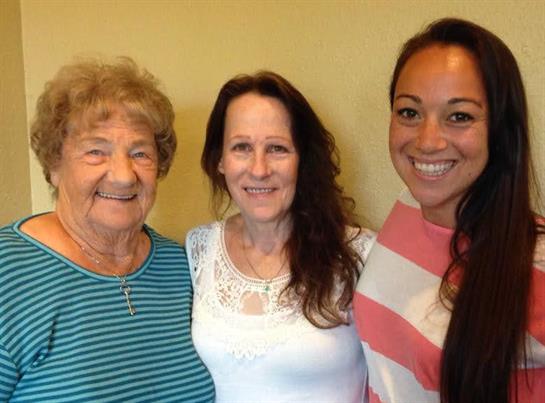 Three women smile at the camera, showing a strong family bond in a cozy setting.