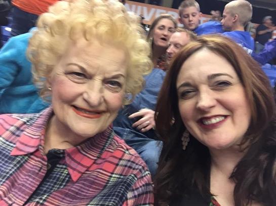 Two women share a joyful moment while watching a sports event surrounded by family.
