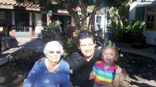 Elderly woman, man, and young girl gather together, enjoying a sunny day in a vibrant garden.