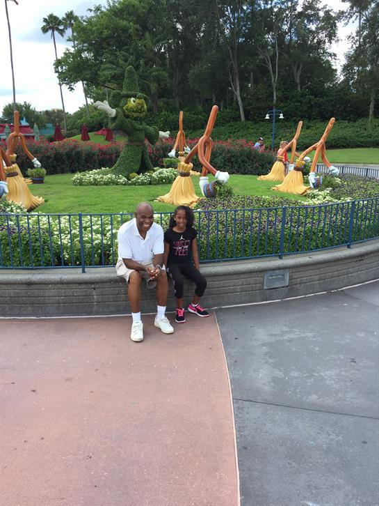 Grandfather and granddaughter sit on a bench, surrounded by vibrant sculptures in a park.