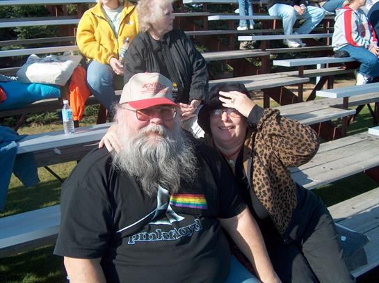 A couple sits closely together on bleachers at a community event, sharing smiles and laughter.