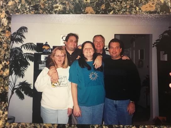 Five friends smile together in a cozy indoor space, enjoying each other's company.