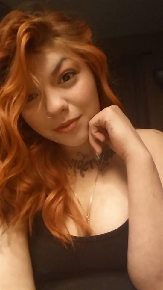 A woman with vibrant red hair rests her chin on her hand, looking contemplative in soft lighting.