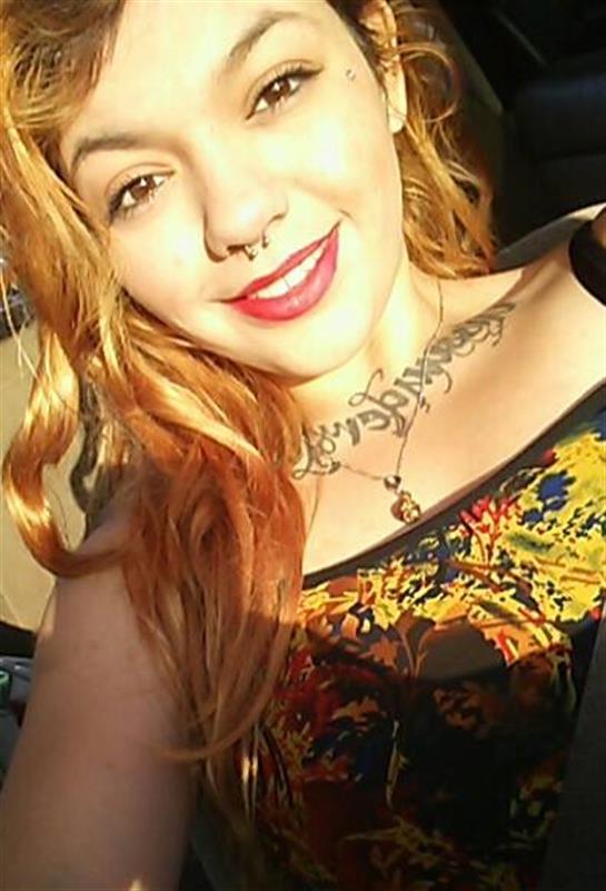 Woman with vibrant hair and tattoos smiles in bright sunlight, showcasing her colorful outfit.