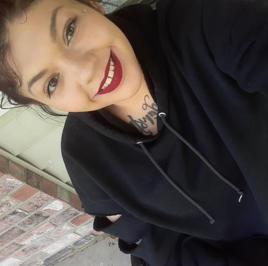 Young woman with dark hair and vibrant lipstick smiles while seated outdoors.