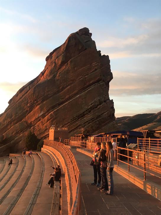 Group of visitors enjoying a beautiful sunset at Red Rocks Amphitheatre during the evening.