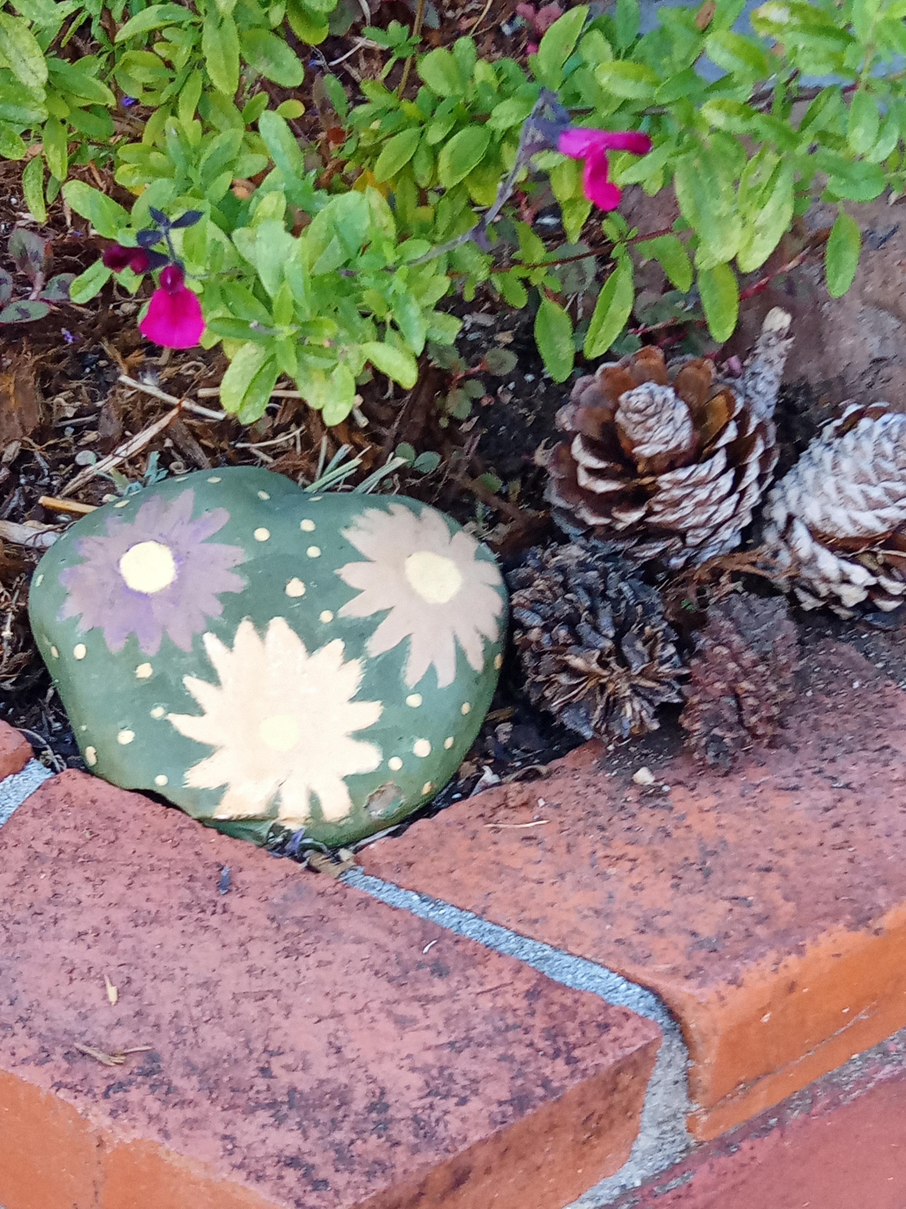 A rock with flowers and pine cones next to a brick wall