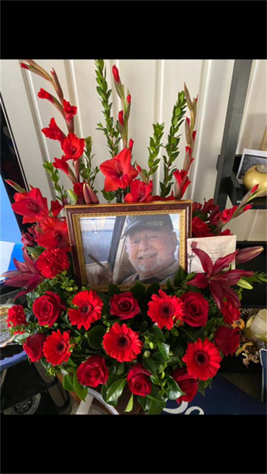A vibrant arrangement of red flowers surrounds a framed portrait, honoring a beloved individual.