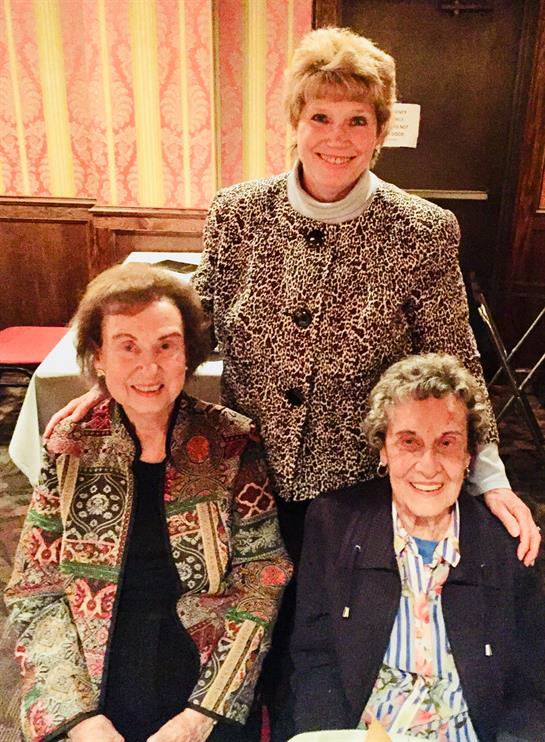 Three women smile together in a warm, inviting space while enjoying each other's company.