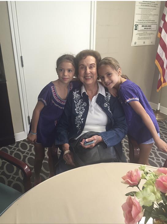 Two girls smile while cuddling with an older woman in a welcoming indoor setting.