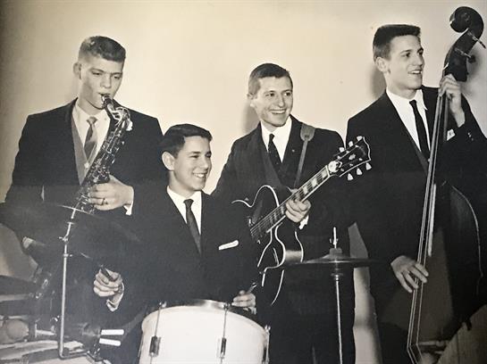 Four musicians play instruments in a vintage studio setting, showcasing their talent and style.