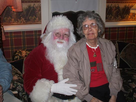 A senior woman sits beside Santa, enjoying a joyful moment during a holiday gathering.