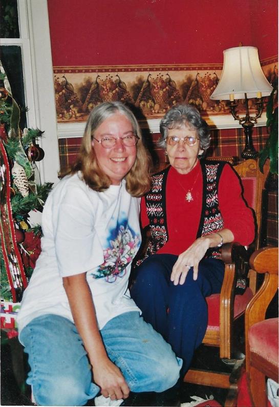 Two women share smiles in a decorated living room, surrounded by Christmas decor and warm ambiance.