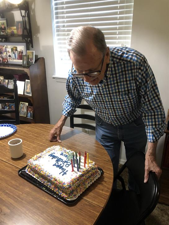 Elderly gentleman leans forward to blow out candles on a birthday cake in a warm home atmosphere.