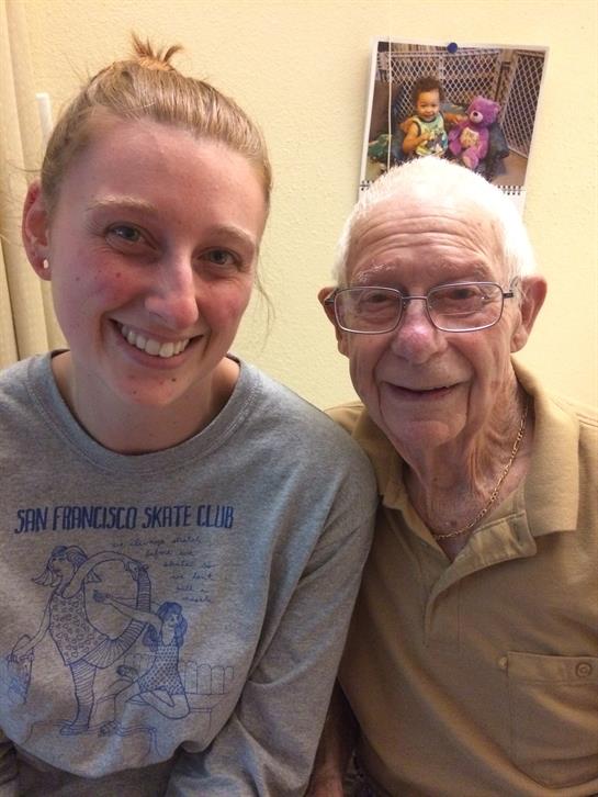 A young woman and an elderly man are smiling happily together in a warm indoor environment.