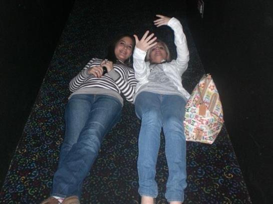 Two friends enjoy a playful moment lying on the floor in a dimly lit indoor area.