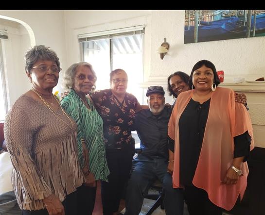 A joyful group of older adults comes together in a warm living room, sharing smiles and laughter.