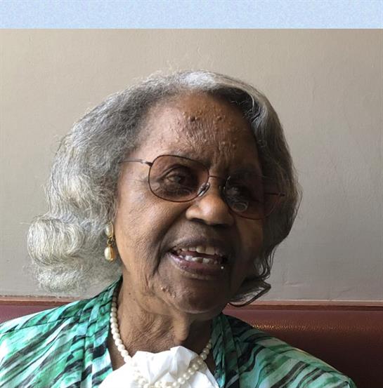 An elegant elderly woman with silver hair and glasses shares a joyful moment, smiling while seated.