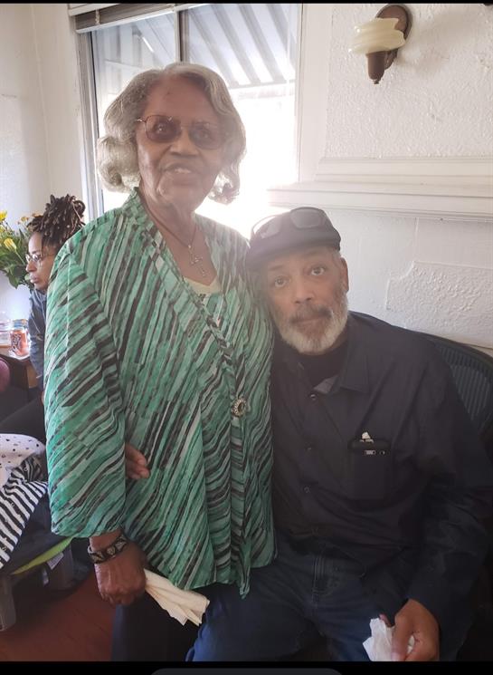 Two elders greet the camera with smiles, enjoying their time together at a social gathering.